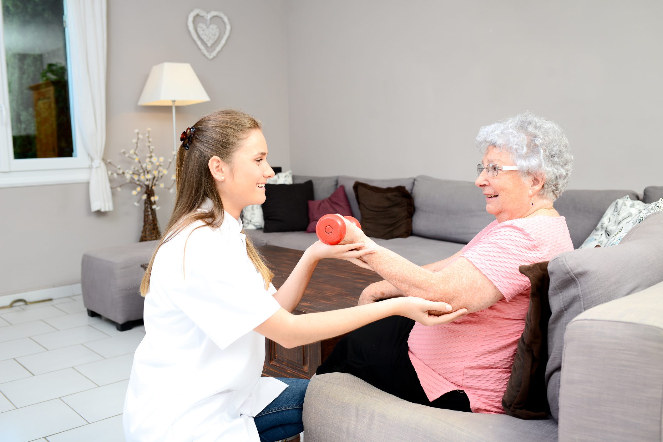 Senior woman doing physical therapy with caregiver using light dumbbell.