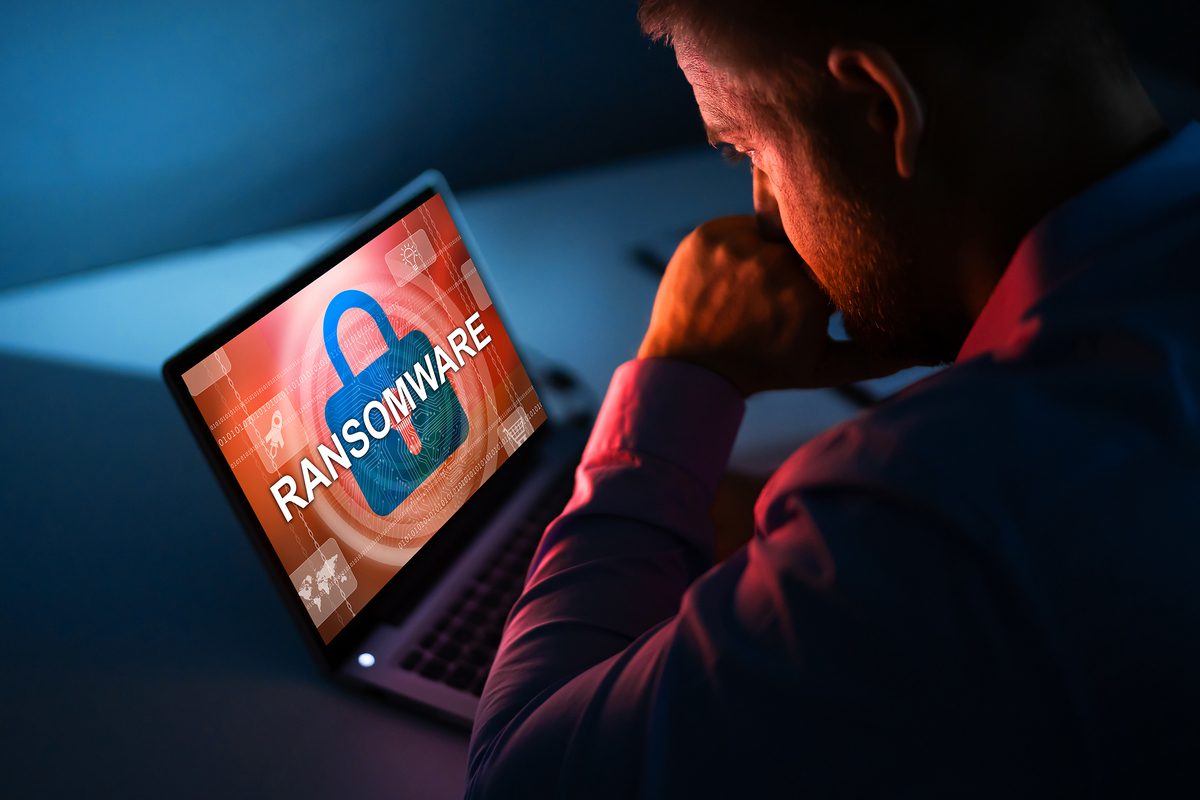 Man looking at laptop screen displaying ransomware alert with padlock graphic.