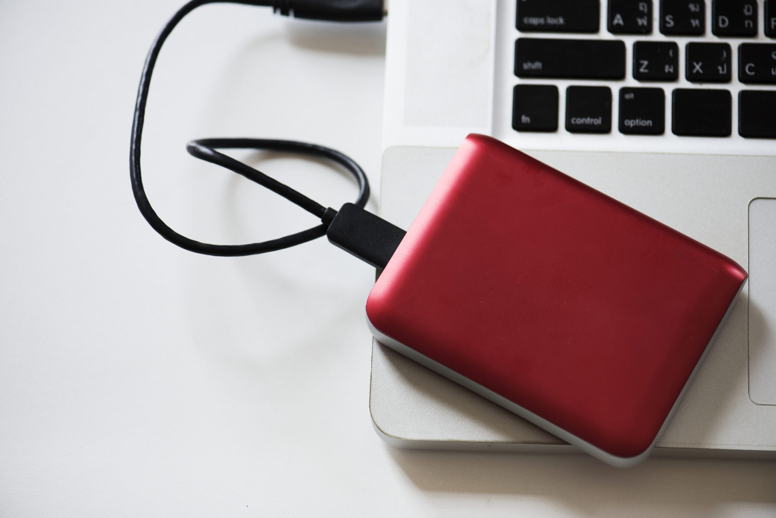 Red external hard drive connected to a laptop for data backup.