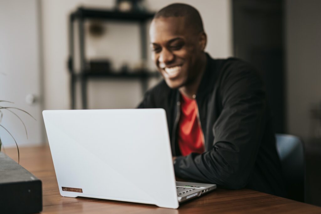 Smiling man using a laptop while working remotely in a modern home office.