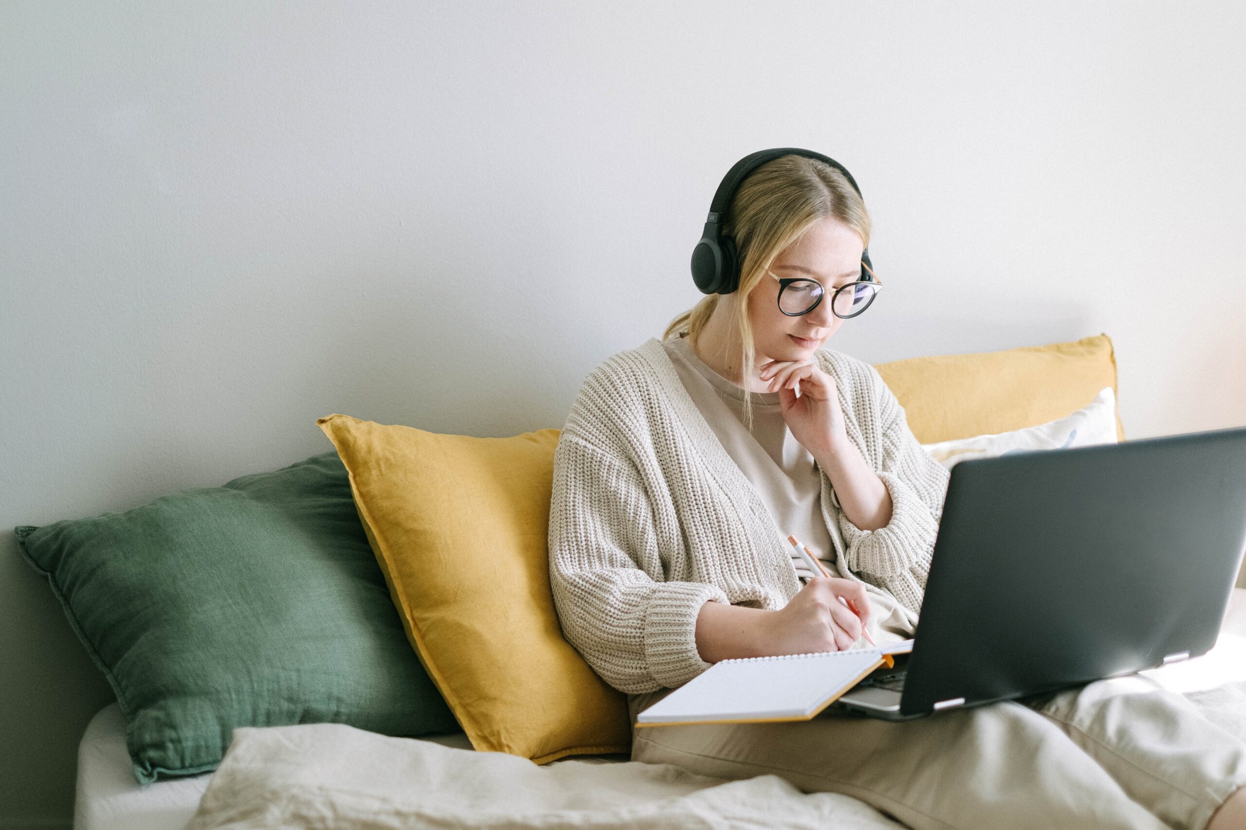 Woman attending an online webinar while taking notes on a laptop from home.