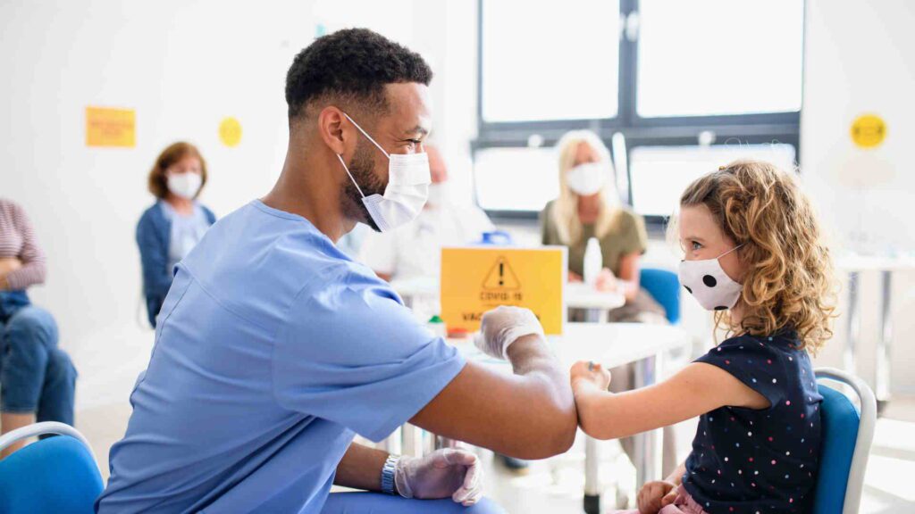 Doctor administering vaccine to child during pandemic safety protocols in medical facility.