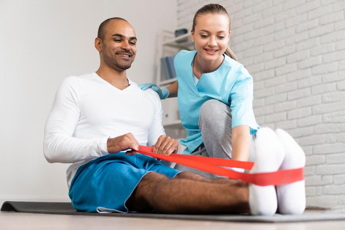 Physiotherapist helping a male patient with resistance band exercises during rehabilitation.
