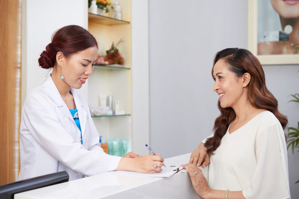 Receptionist assisting a patient with check-in paperwork at a healthcare clinic.