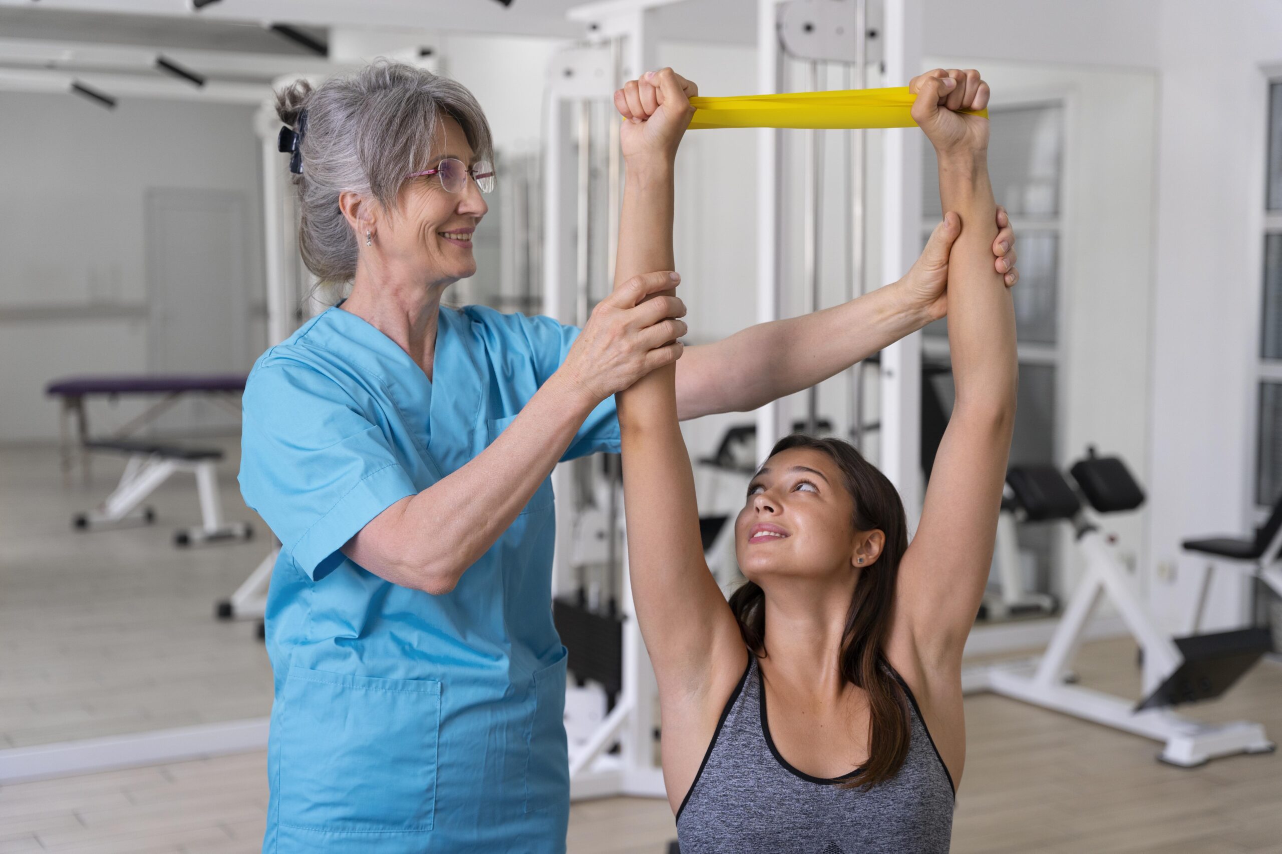 Physiotherapist assisting a young woman with shoulder exercises using a resistance band.