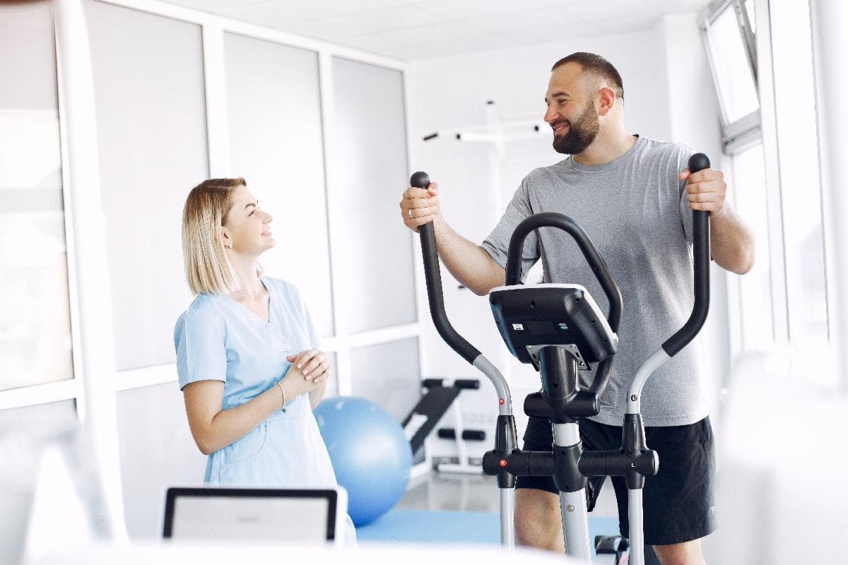 Physiotherapist guiding a male patient during rehabilitation on an exercise bike.