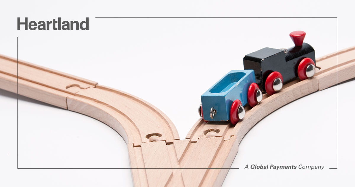 Heartland logo with wooden toy train on a split railway track symbolizing business direction choices.