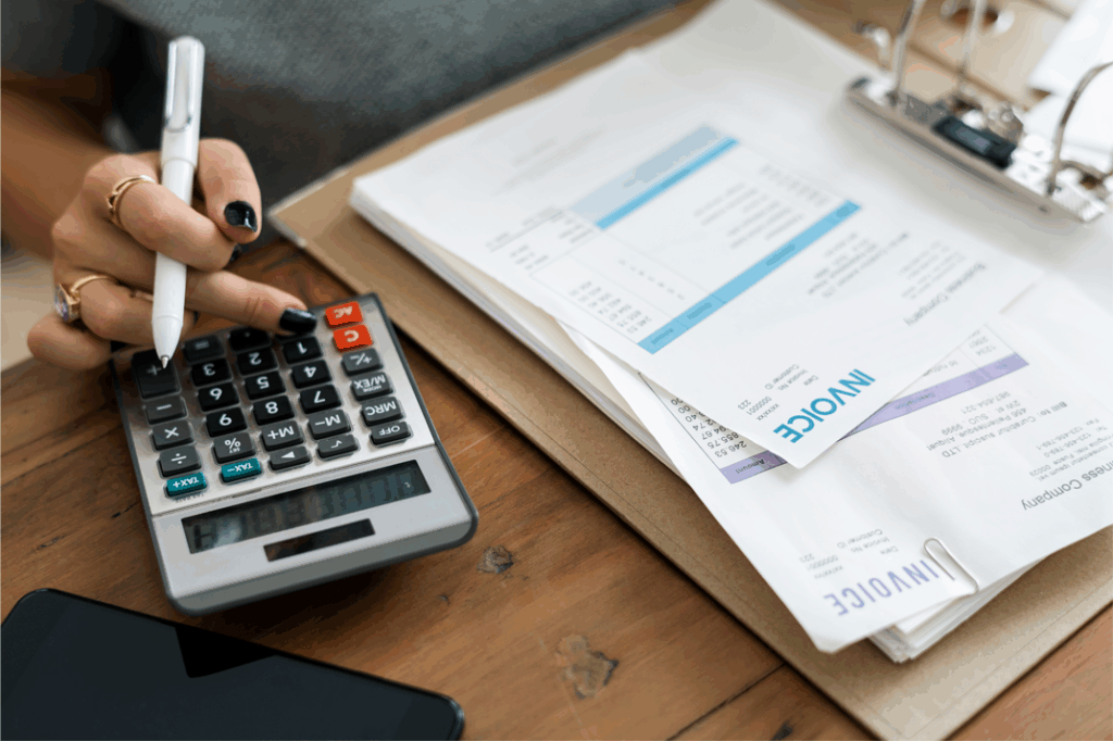 Close-up of a person using a calculator with invoices and billing documents on a desk.