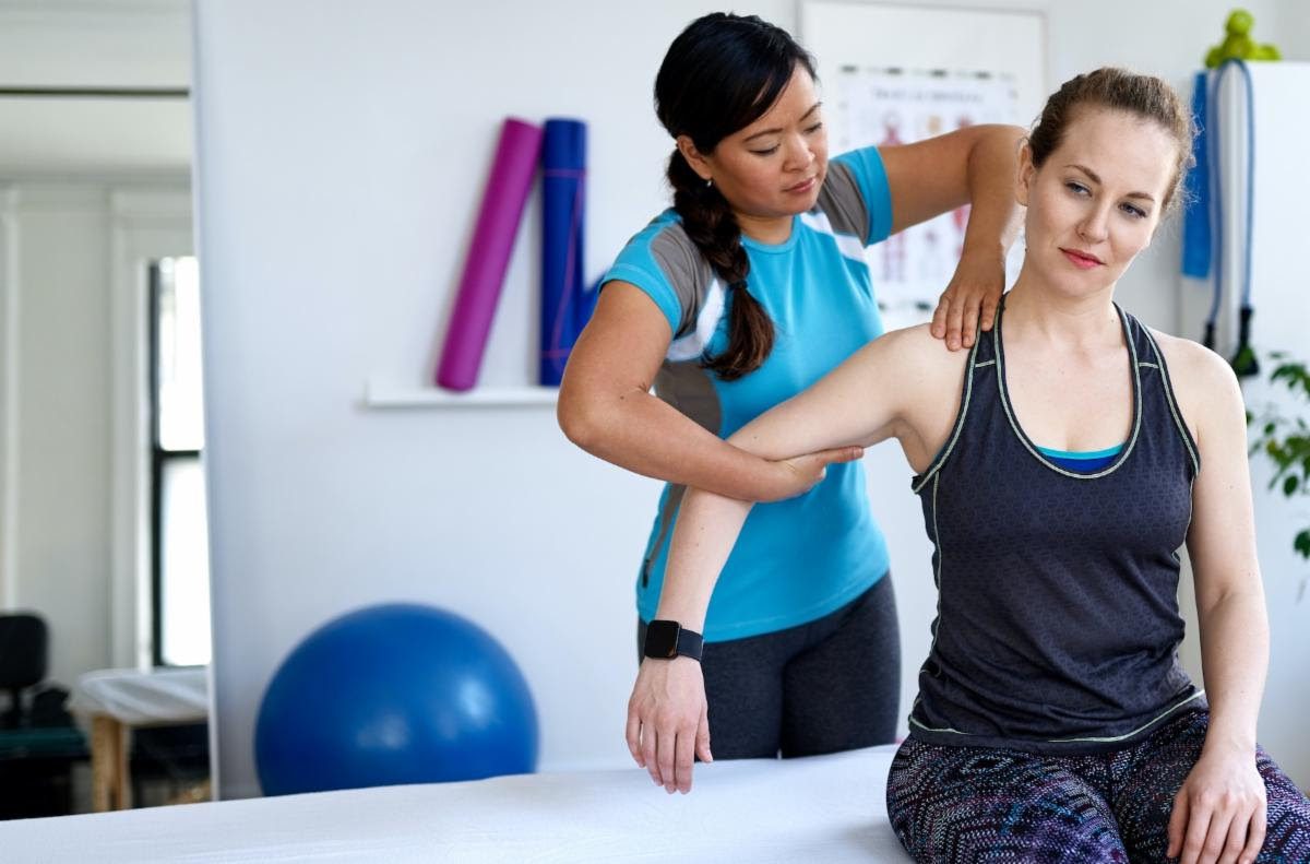 Physical therapist helping a woman stretch her shoulder during a rehabilitation session.