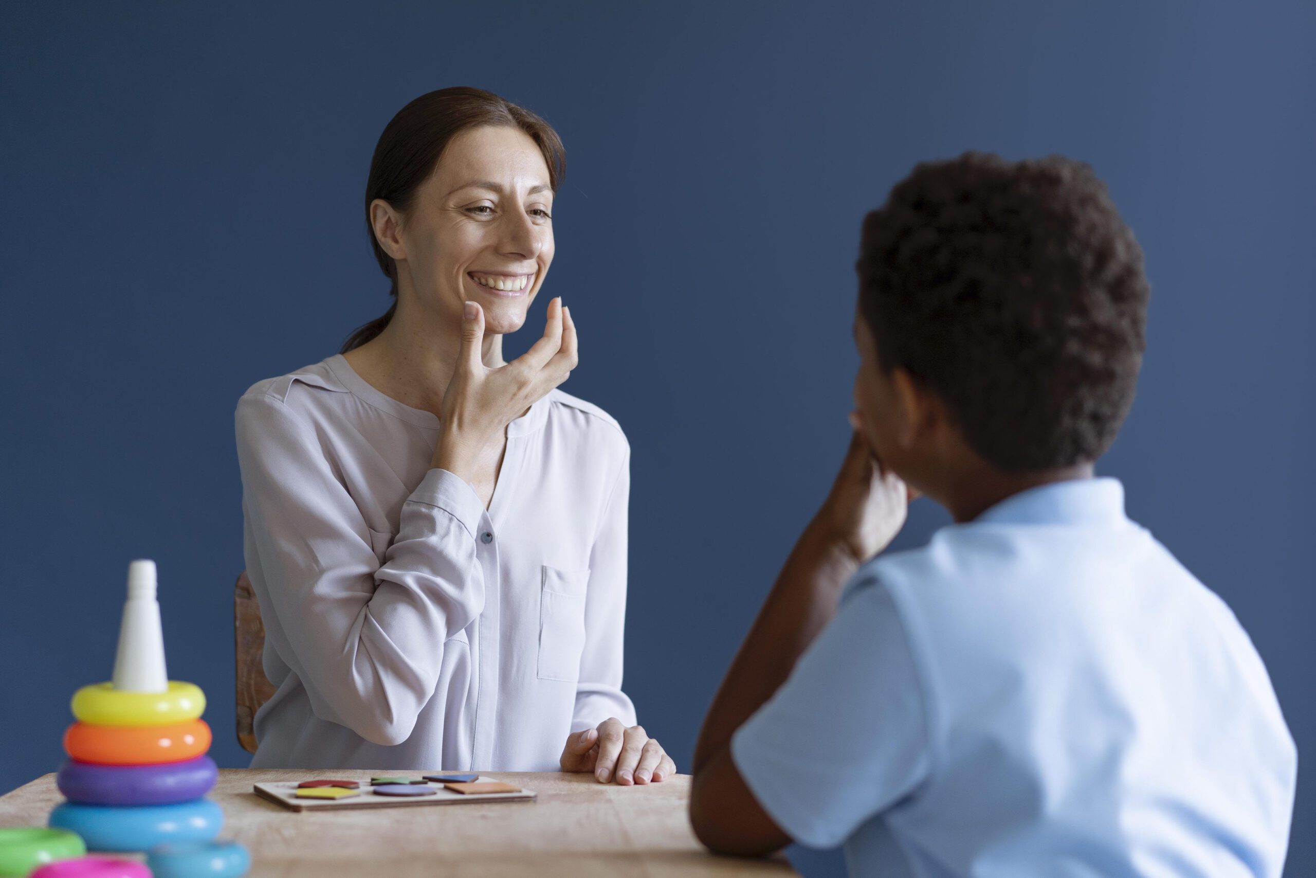 Speech therapist teaching pronunciation exercises to a young boy during therapy session.