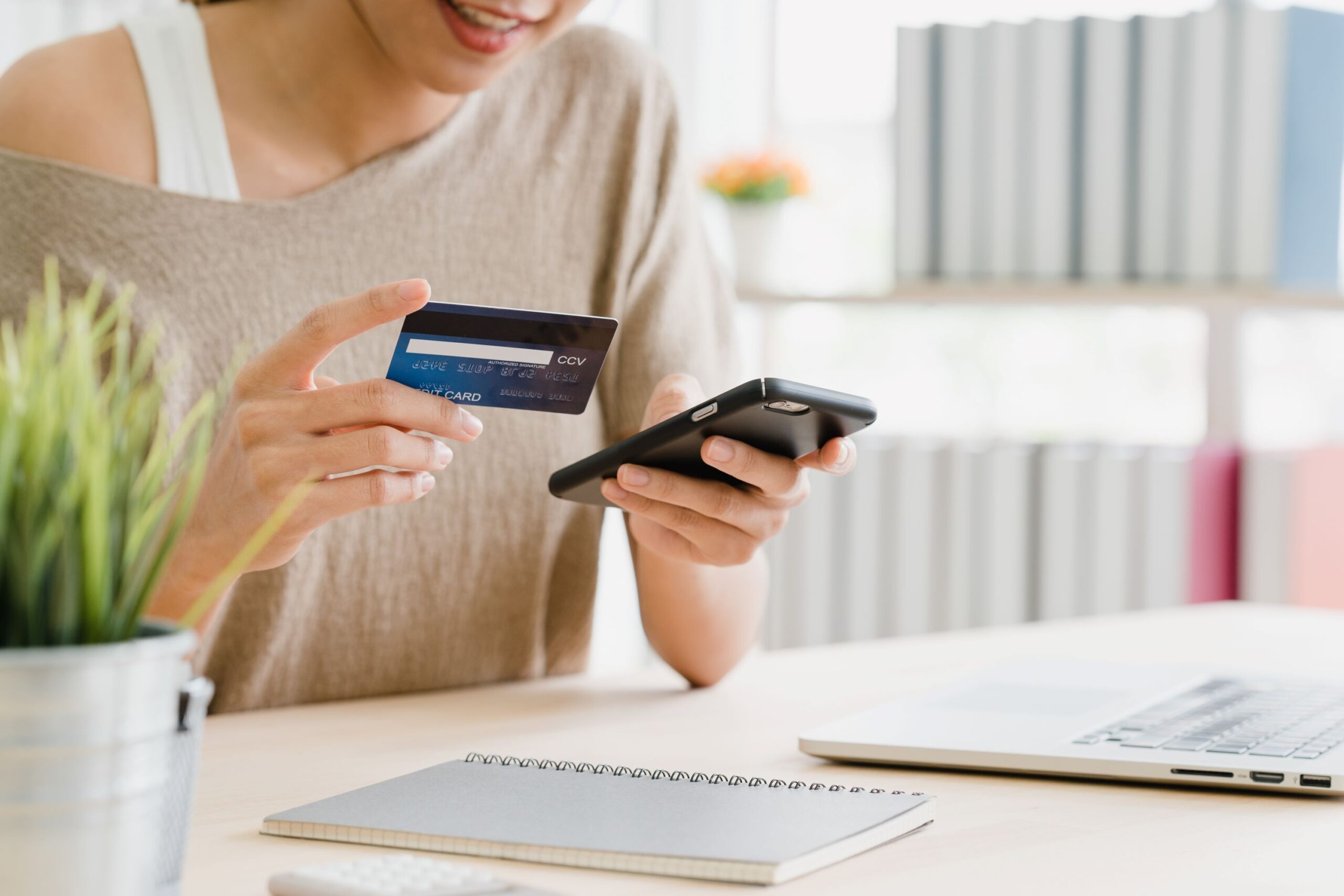 Person making an online payment using credit card and smartphone at home office desk.