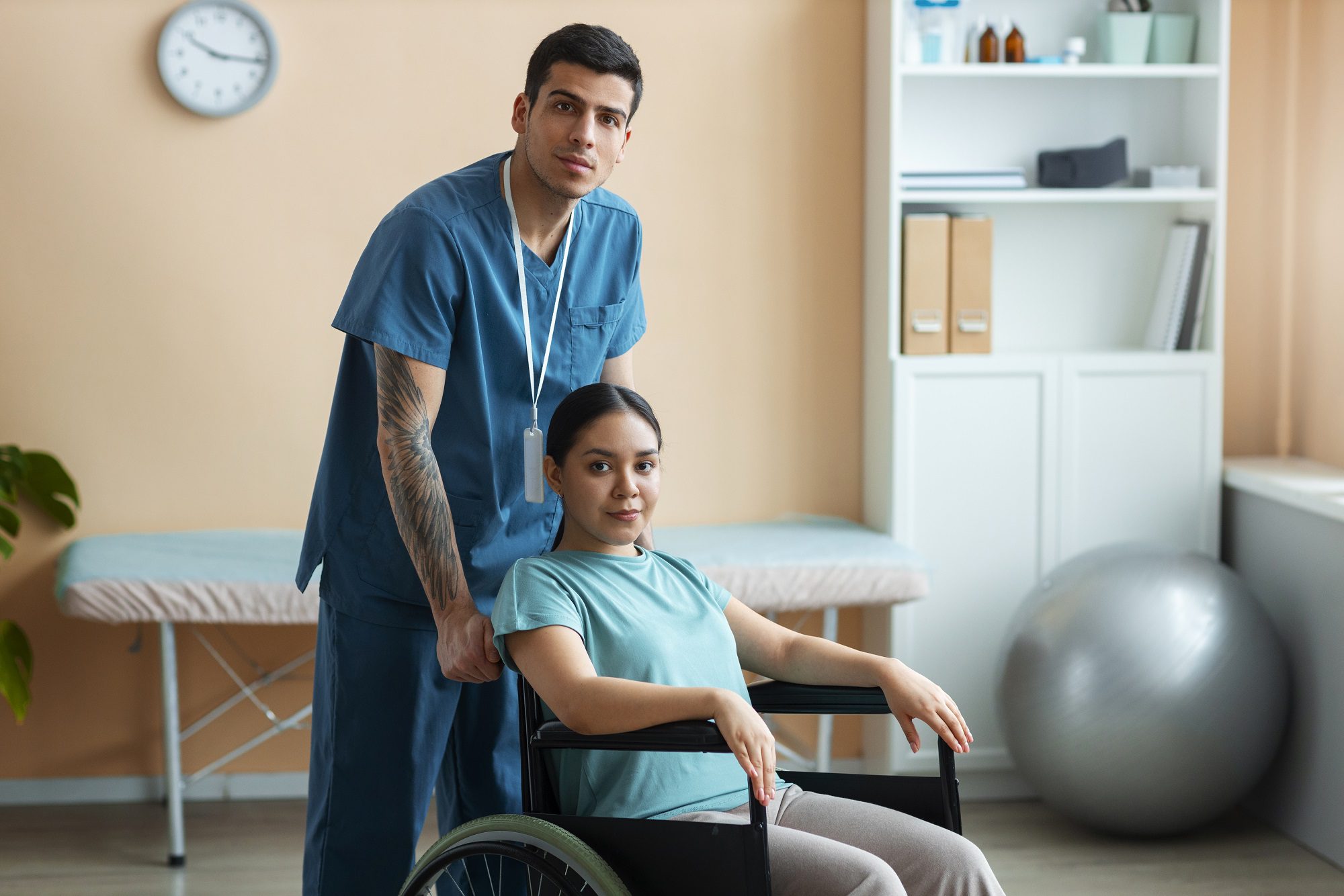 Physiotherapist standing beside female patient in wheelchair during rehabilitation session.