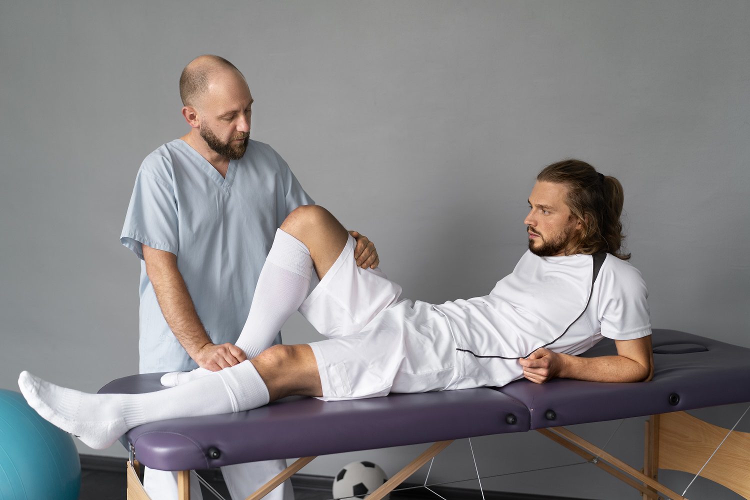 Physiotherapist examining injured athlete’s knee during sports rehabilitation session.