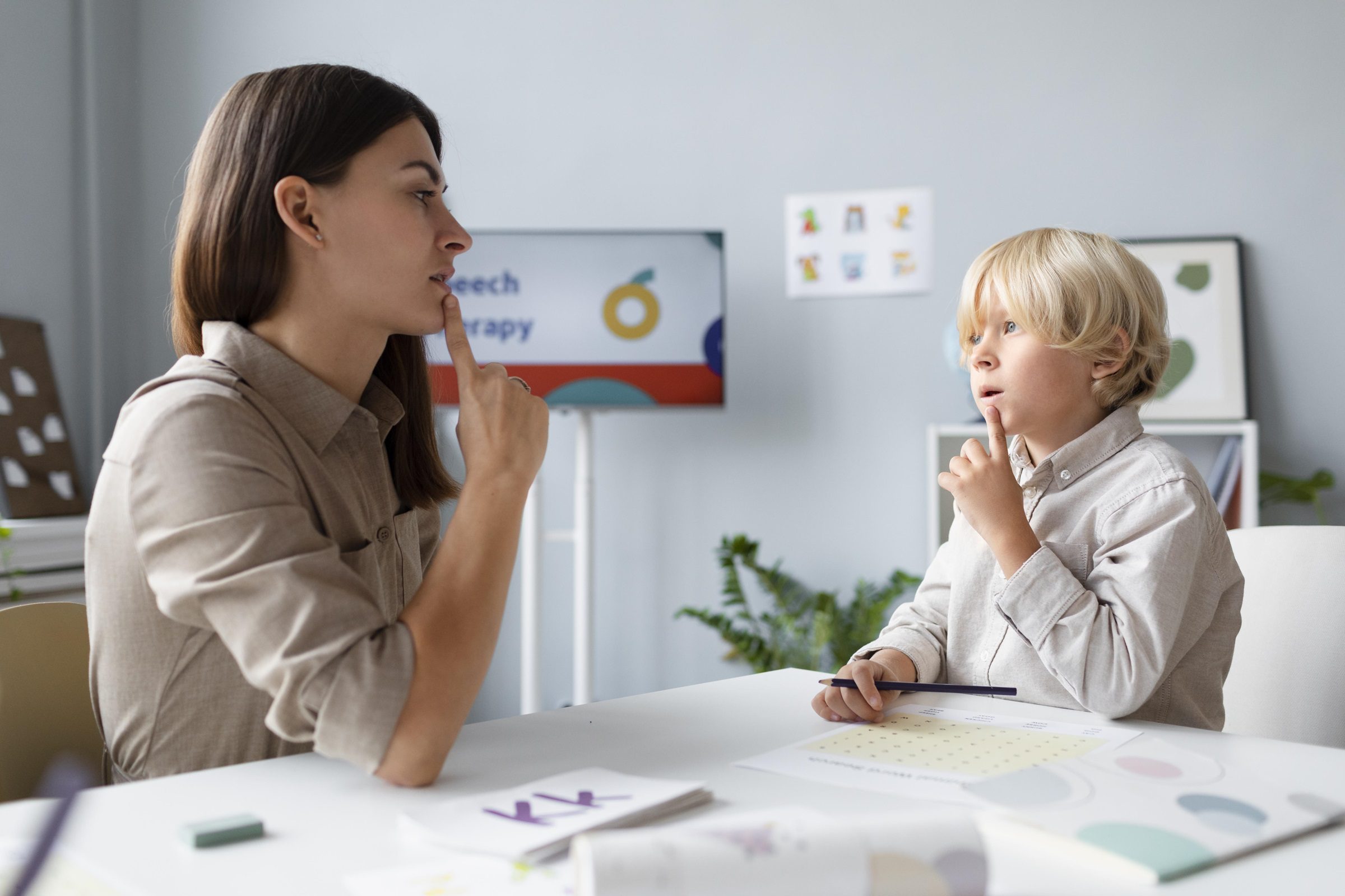 Speech therapist working with young boy on pronunciation exercises in therapy session.