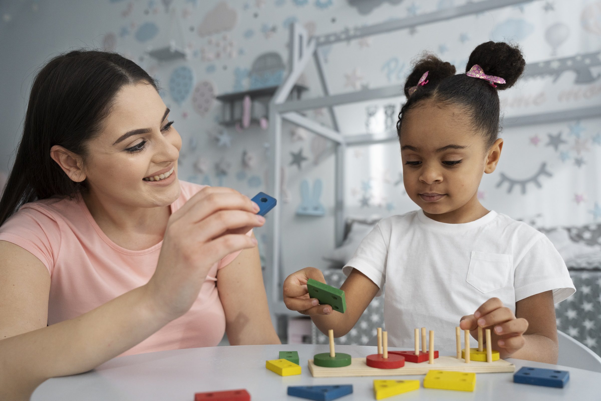 Child engaging in learning activity with educator using wooden shape and colour blocks.