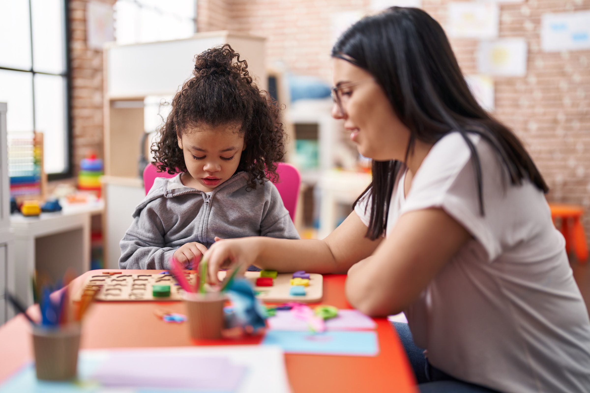Educator helping young girl with educational puzzle activities at classroom table.