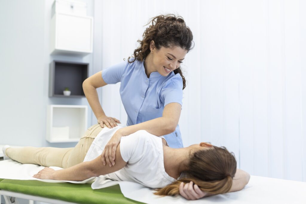 Smiling therapist performing spinal alignment on woman lying on treatment table.